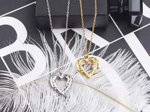 Macro view of textured heart pendants in gold and silver on soft white feathers