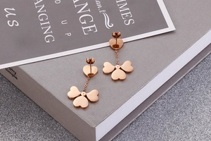 Detailed close-up of rose gold heart and clover dangle earrings on a gray magazine