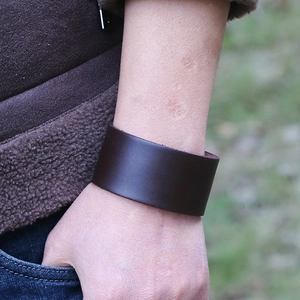 Close-up of wide dark brown smooth leather bracelet worn on a wrist outdoors