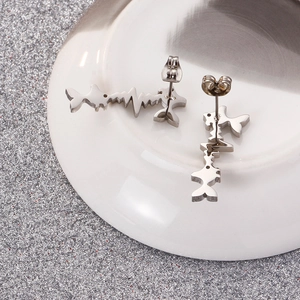 Modern silver stainless steel fish and heartbeat stud earrings on white ceramic tray