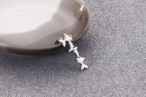 Macro shot of silver heartbeat fish tail stud earrings on a textured ceramic surface