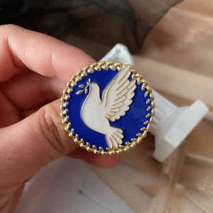 Macro detail of peace dove enamel brooch with a textured gold border and olive branch
