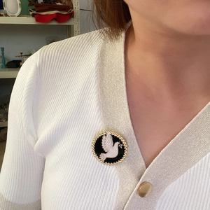 Detail of vintage peace dove enamel brooch with gold beads on white knit cardigan
