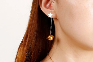 Detail of gold star and planet drop earrings worn by a model in soft lighting