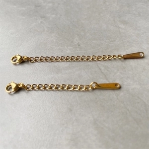 Detail of gold stainless steel extension chains with lobster clasps on marble background