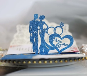 Close-up of a blue glitter wedding cake topper with Mr & Mrs silhouette and rings