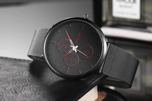 Macro shot of black quartz watch with red hands and silver mesh strap on leather