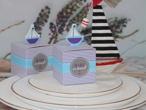 Detail of nautical blue striped candy gift box with a sailboat topper on white plates