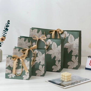 Green paper gift bags with white floral prints and gold ribbon handles in four sizes