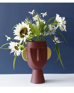 Vaso artistico a forma di viso con dettagli dorati e composizione di fiori bianchi