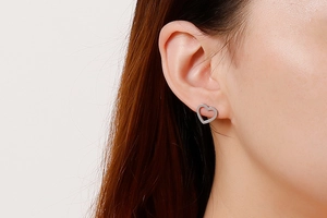 Close-up of polished silver hollow heart stud earrings on a model's ear