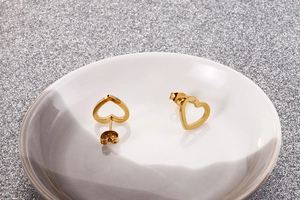 Detailed view of gold heart-shaped hollow stud earrings on a white ceramic tray