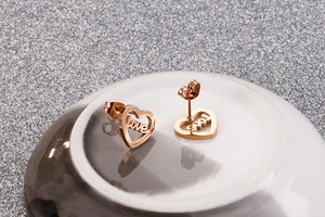 Macro view of rose gold heart earrings with love script on a textured gray background