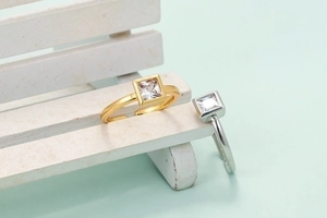 Minimalist square zircon rings in gold and silver finishes on a mini white bench display