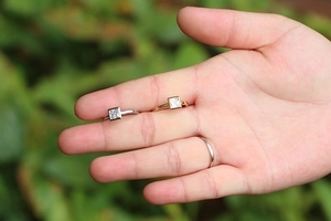 Gold and silver copper rings with square zircon stones held in hand against greenery