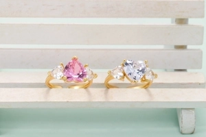 Adjustable golden rings with pink and clear heart shaped crystals on a wooden bench