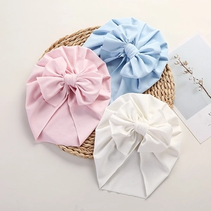 Mesh baby turban hats with large bows in pink blue and white on woven mat