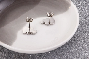 Close-up of polished elephant-shaped steel stud earrings on a ceramic tray