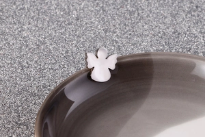 Macro detail of a silver angel-shaped stainless steel stud earring on a ceramic edge