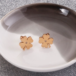 Elegant rose gold four-leaf clover stud earrings with white crystal in ceramic tray