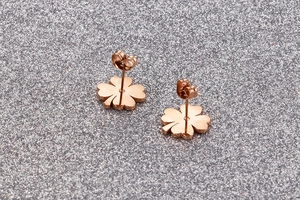 Macro detail of rose gold four-leaf clover stud earrings on a grey glitter surface