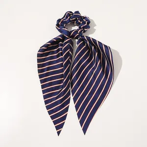 Macro detail of the smooth satin finish and diagonal red stripes on the navy ribbon scrunchie