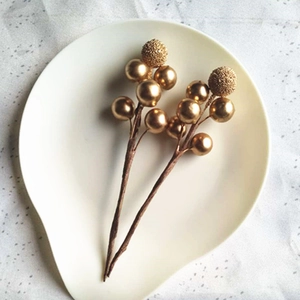 Close-up of golden faux berry stems with metallic glitter on a white ceramic plate