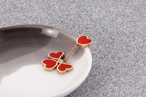 Detail of rose gold heart earrings with red enamel and lucky clover-shaped pendant