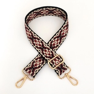 Detail of burgundy geometric jacquard woven bag strap with gold metal lobster clasps