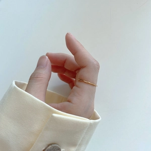 Close-up of minimalist gold wave ring on hand showing delicate irregular design