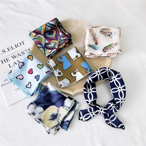 Flat lay of multiple printed small square silk scarves in various patterns and colors