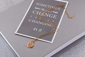 Detailed close-up of golden rose hollow pendant necklace resting on a grey book surface