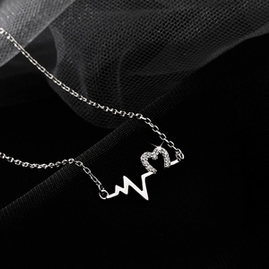 Silver heartbeat wave necklace with diamond heart pendant on a premium black fabric background