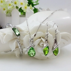Elegant green crystal necklace, earrings, and bracelet jewelry set on white floral decor