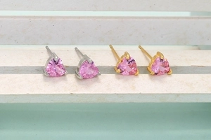 Pink heart stud earrings with silver and gold bases on a white wooden background