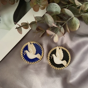 Detail of round enamel peace dove brooches with gold braided borders on silk