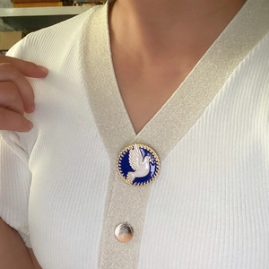Vintage gold peace dove enamel brooch with blue background on a white knit sweater