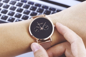 Gros plan d'une montre à bracelet milanais en or rose avec cadran noir sur le poignet