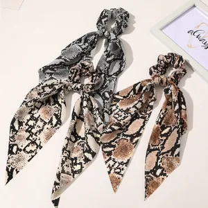 Detail shot of two snake print satin hair scrunchies with long ribbons on white surface