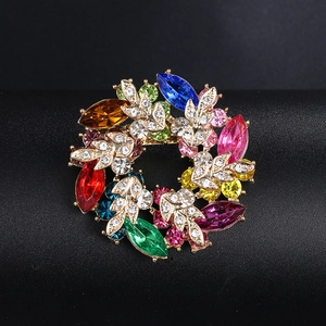 Detailed macro view of a colorful rhinestone wreath brooch with golden metal leaf accents