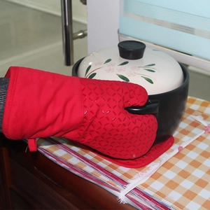 Detail of red silicone heat resistant oven mitt lifting a ceramic lid on checkered table