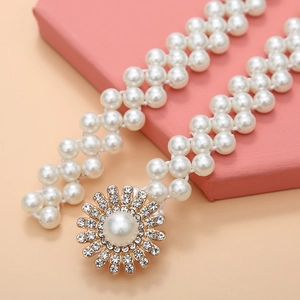 Detail view of pearl and rhinestone floral buckle on elastic gold chain belt