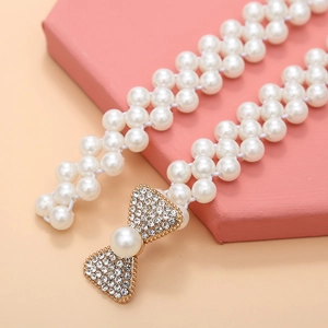 Macro detail of white pearl waist chain featuring a sparkling rhinestone bow buckle
