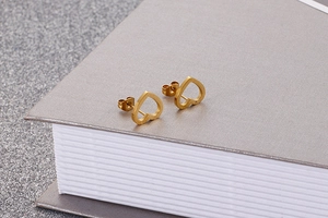 Detail view of hollow heart stud earrings in 18k gold finish on a grey book background