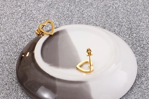 Close-up of golden hollow heart earrings displayed on white ceramic plate with glitters