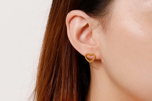 Close-up of a woman wearing gold hollow heart stud earrings in polished titanium steel