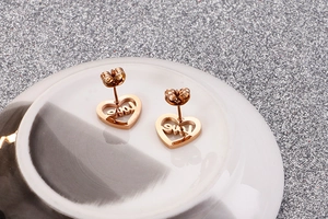 Macro shot of rose gold heart-shaped stud earrings with Love engraving on ceramic
