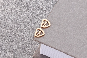 Macro shot of rose gold heart earrings with love engraving on a grey book edge