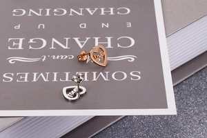 Detailed close-up of rose gold and silver heart stud earrings with love cut-out design