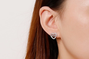 Close-up of a silver heart-shaped stud earring with love engraving on a female ear